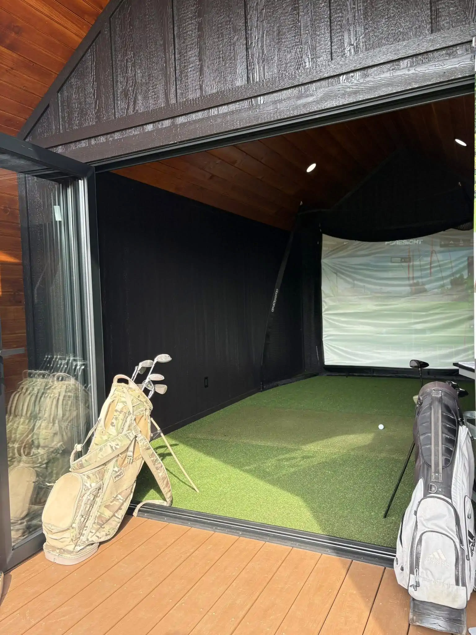 Interior of a shed set up as a golf simulator with a screen and projector.